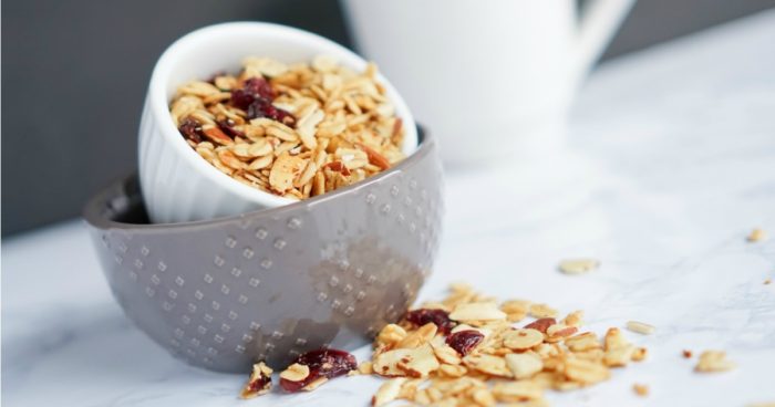 Granola in a bowl next to a cup of coffee features the Baked Cranberry Almond Granola Recipe.