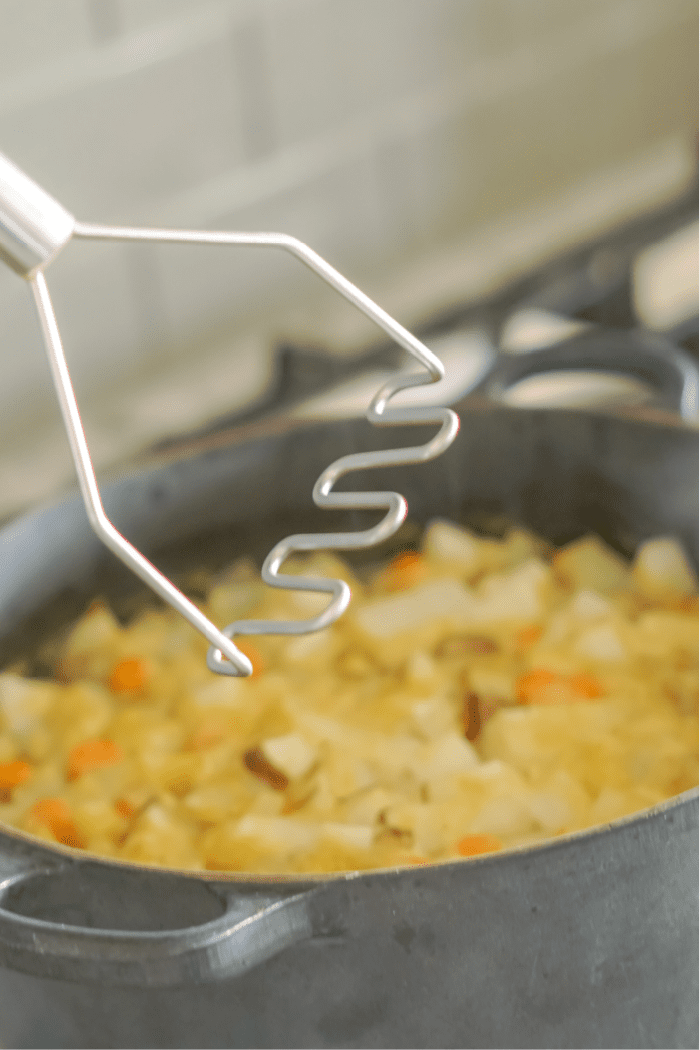 Potato masher in a pot of soup.