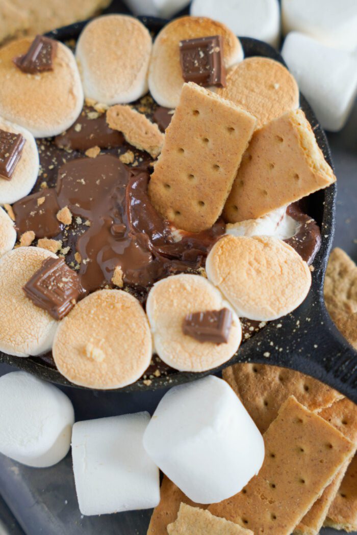 A skillet of melted chocolate with marshmallows and graham crackers.