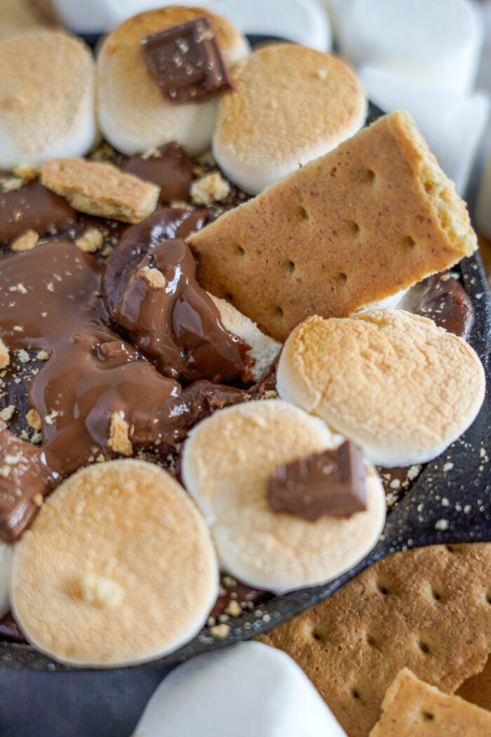 A graham cracker being dipped into melted chocolate and marshmallows.