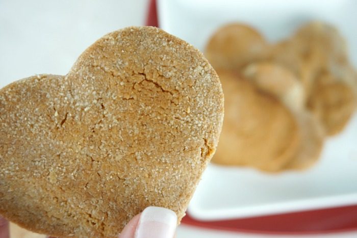 A person holding a heart-shaped homemade dog treat on a plate.