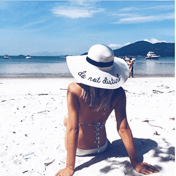 A woman sitting on the beach wearing a cute white sun hat.