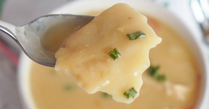 A spoon is holding a bowl of homemade chicken and dumplings soup.