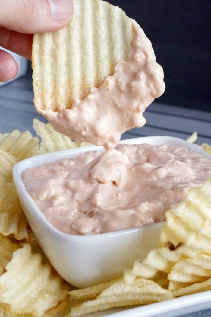 A person dipping chips into a bowl of easy cream cheese pink dip.