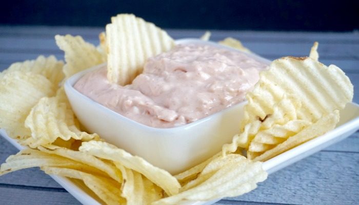 A bowl of easy cream cheese pink dip with chips on a white plate.