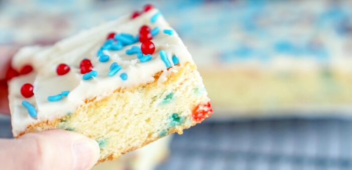 A person holding a homemade sugar cookie bar with sprinkles on it.