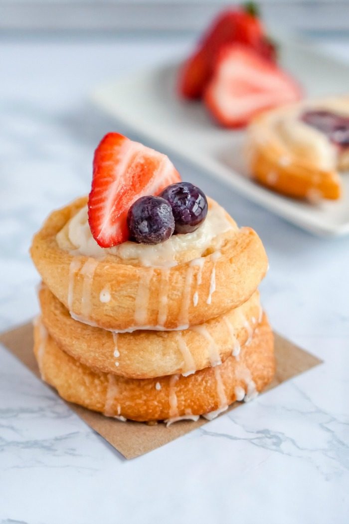 A stack of pastries, part of an easy Crescent Roll Cream Cheese Danish recipe, with berries and icing.