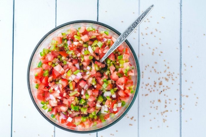 A bowl of easy Pico De Gallo recipe without cilantro with a spoon on a wooden table.