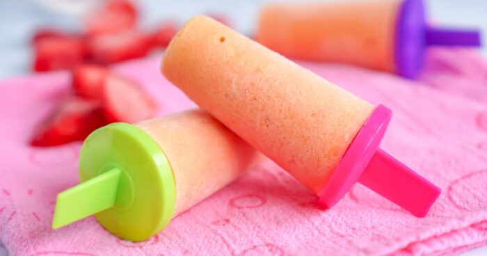 Popsicles with strawberries and mango on a pink towel.