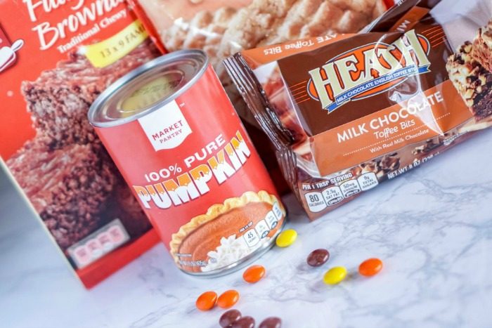 A can of Easy Pumpkin Peanut Butter Brownies, candy, and cookies on a marble countertop.