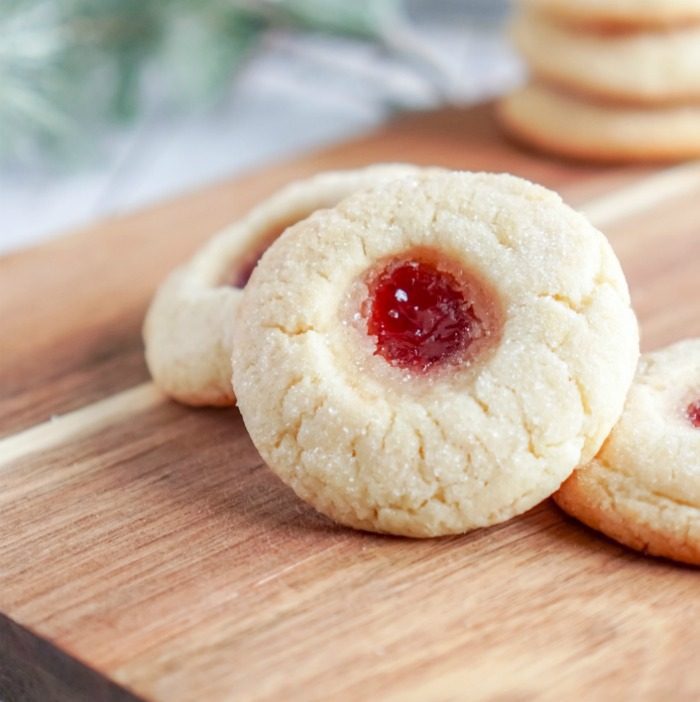 Two Christmas Thumbprint Sugar Cookies with jam on top of a cutting board.