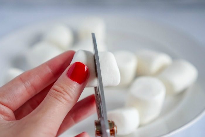 A person cutting up marshmallows on a plate for an easy hot chocolate recipe.