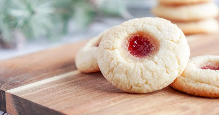 Two Christmas Thumbprint Sugar Cookies with jam on top of a cutting board.