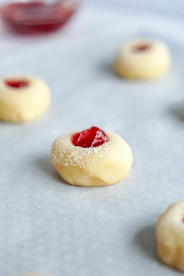 A baking sheet with Christmas Thumbprint Sugar Cookies and jelly on it.