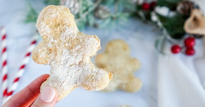 A person holding a homemade gingerbread cookie in front of a Christmas tree.