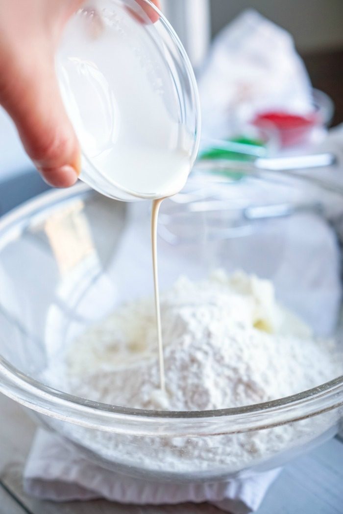 A person pouring milk into a bowl of flour for a Sugar Cookie Dough Dip recipe for Christmas.