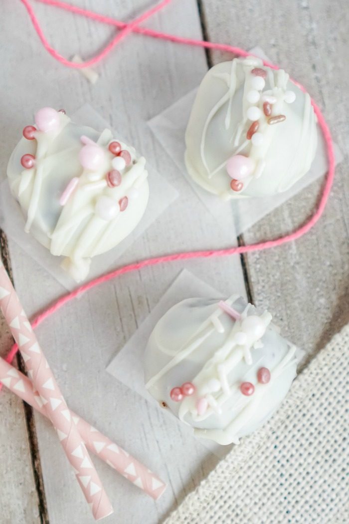 Valentine's day No Bake Oreo Cheesecake Balls with white frosting and pink sprinkles.