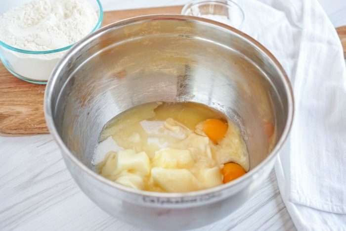 A bowl with flour, eggs, sugar, and butter next to a wooden cutting board for an easy Snickerdoodle recipe without Cream of Tartar.