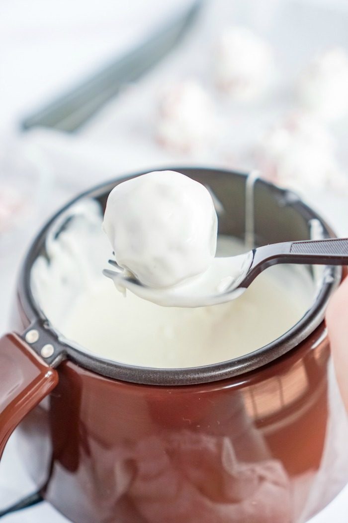 A person pouring whipped cream into a pot for No Bake Oreo Cheesecake Balls.