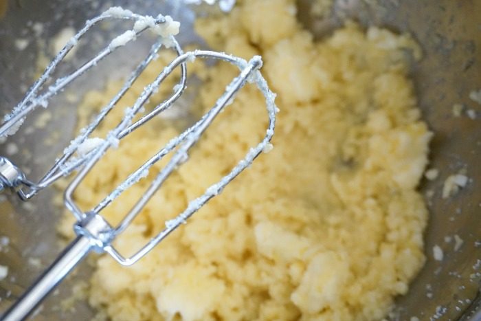 A whisk is being used to mix mashed potatoes in a bowl for a Lemon Sugar Cookies recipe.