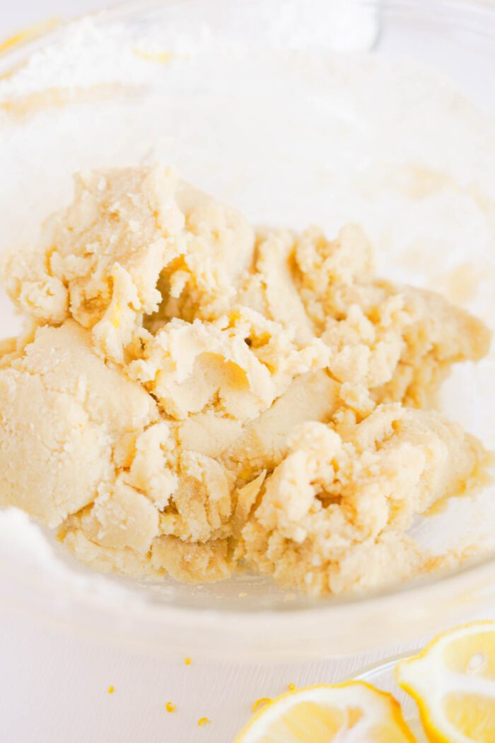 Bowl of lemon sugar cookie dough with visible zest on a white background.
