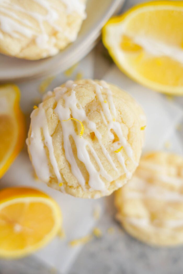 Lemon sugar cookies with white icing and zest on top, surrounded by lemon slices on a marble surface.