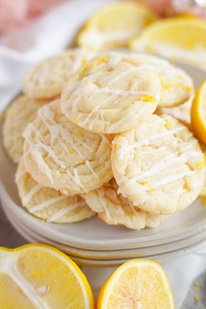 Lemon sugar cookies with white icing on a plate, garnished with fresh lemon slices.