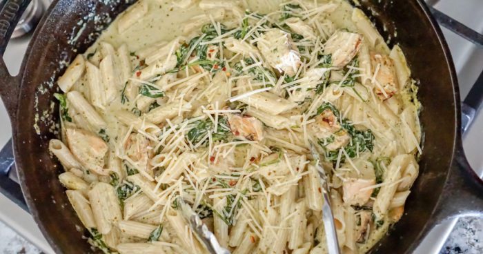 A skillet full of creamy pasta with chicken and spinach.