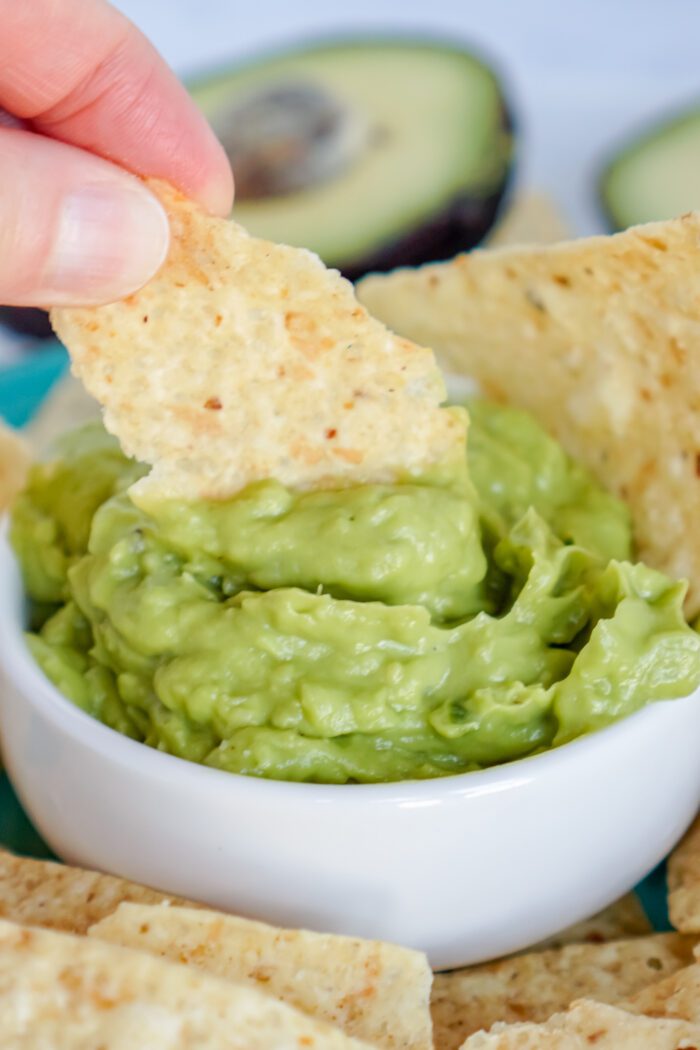 A person dipping tortilla chips into a bowl of guacamole salsa.