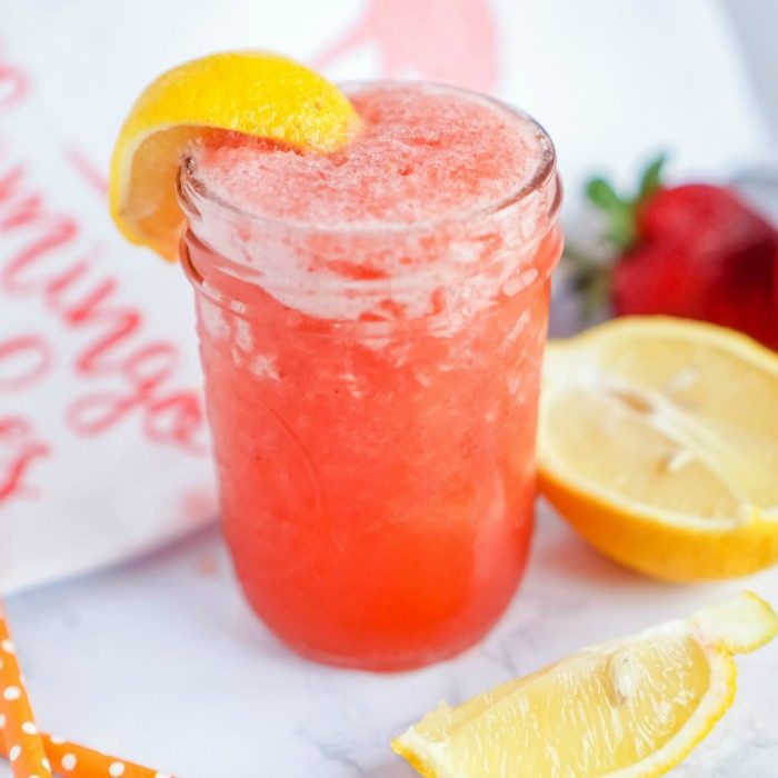 A glass of strawberry lemonade with lemon wedge.