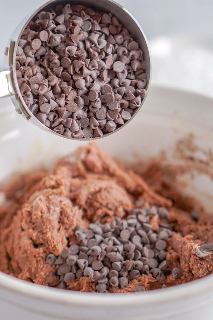 Chocolate chips being poured into cookie dough.