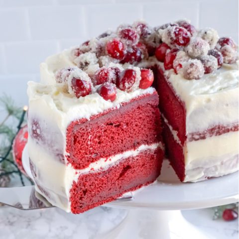 A red velvet cake with cream cheese frosting and sugared cranberries.