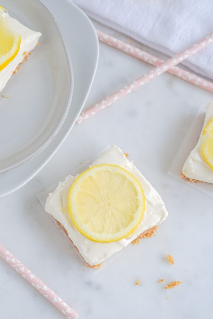 A square lemon cheesecake bar garnished with a lemon slice.