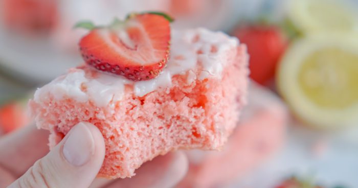 A close-up of a hand holding a piece of strawberry cake.