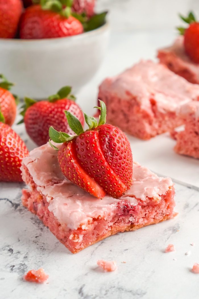 A square of strawberry poke cake with fresh strawberries.