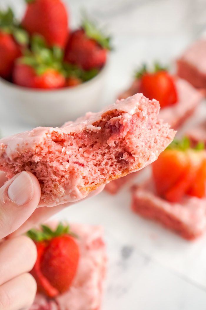 A hand holding a piece of strawberry cake.