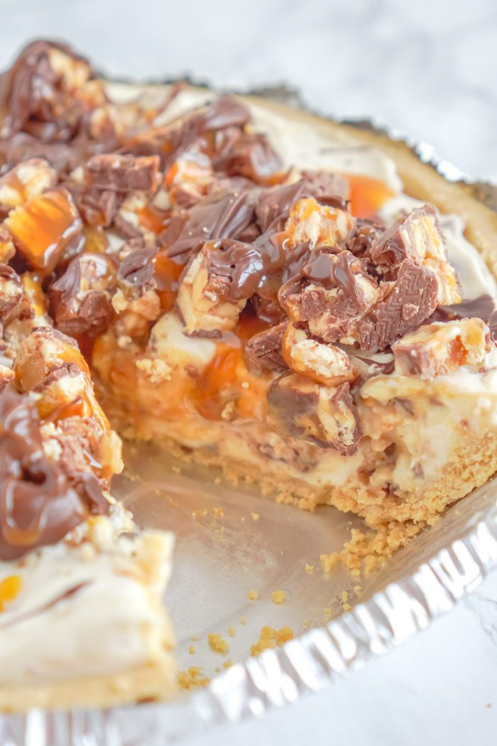 A pie with a graham cracker crust, a layer of chocolate, a layer of caramel, and a layer of whipped cream.