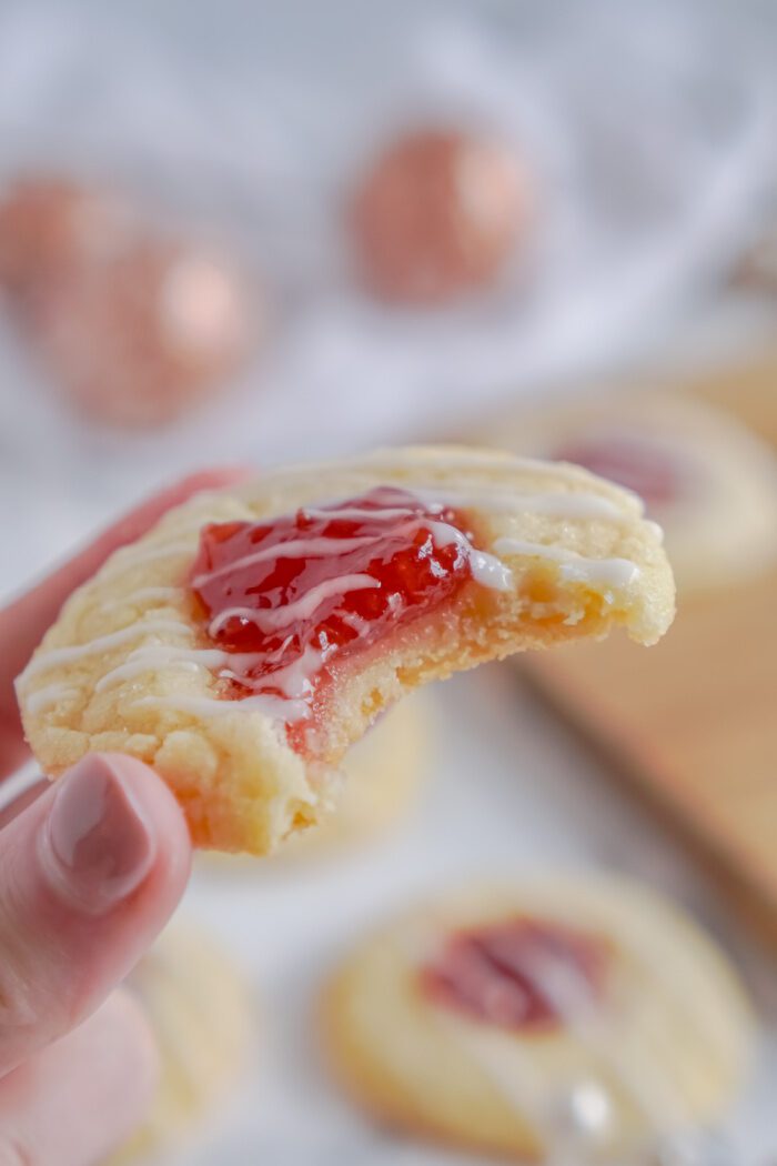 Someone Holding a Thumbprint Cookie With Bite Taken Out