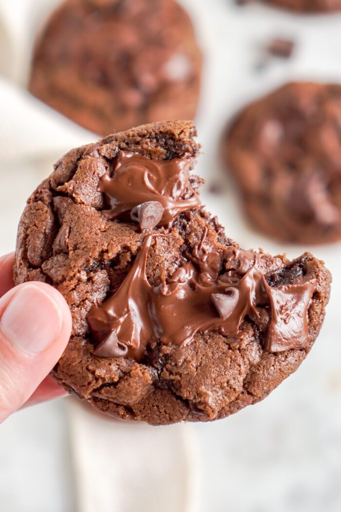 Someone holding a Bakery Style Triple Chocolate Cookie with a bite taken out of it