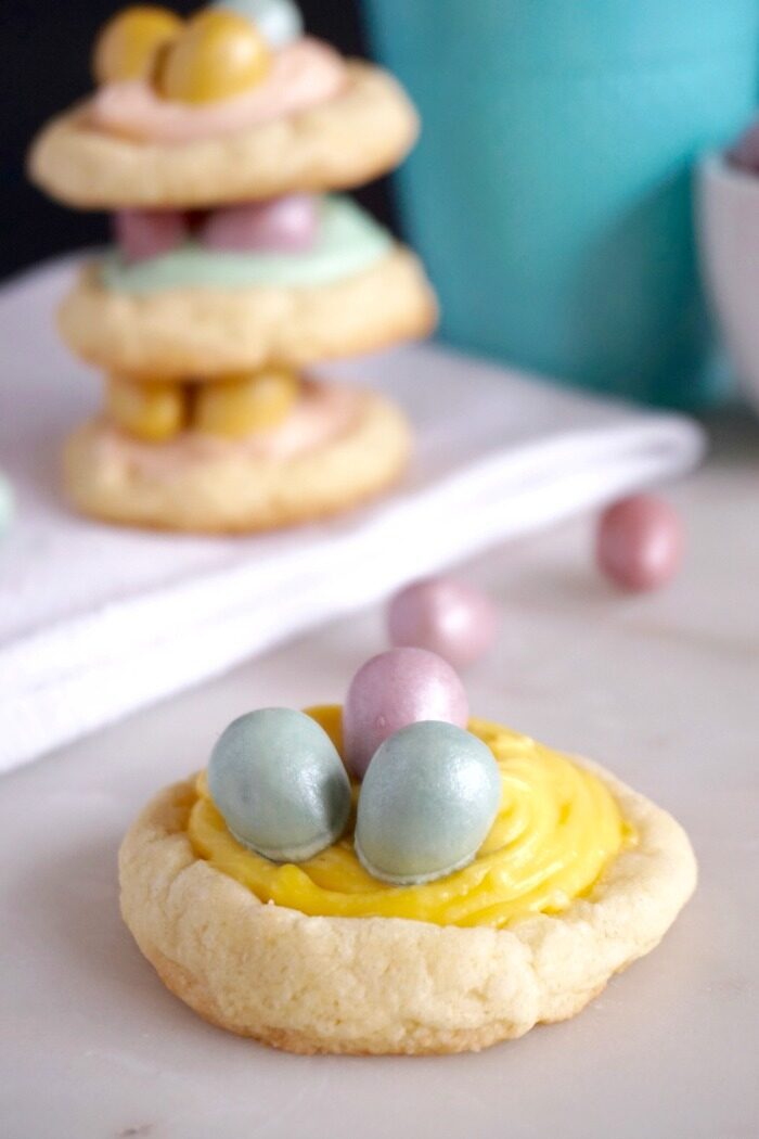 A close-up image of a sugar cookie decorated with yellow frosting and candy eggs.