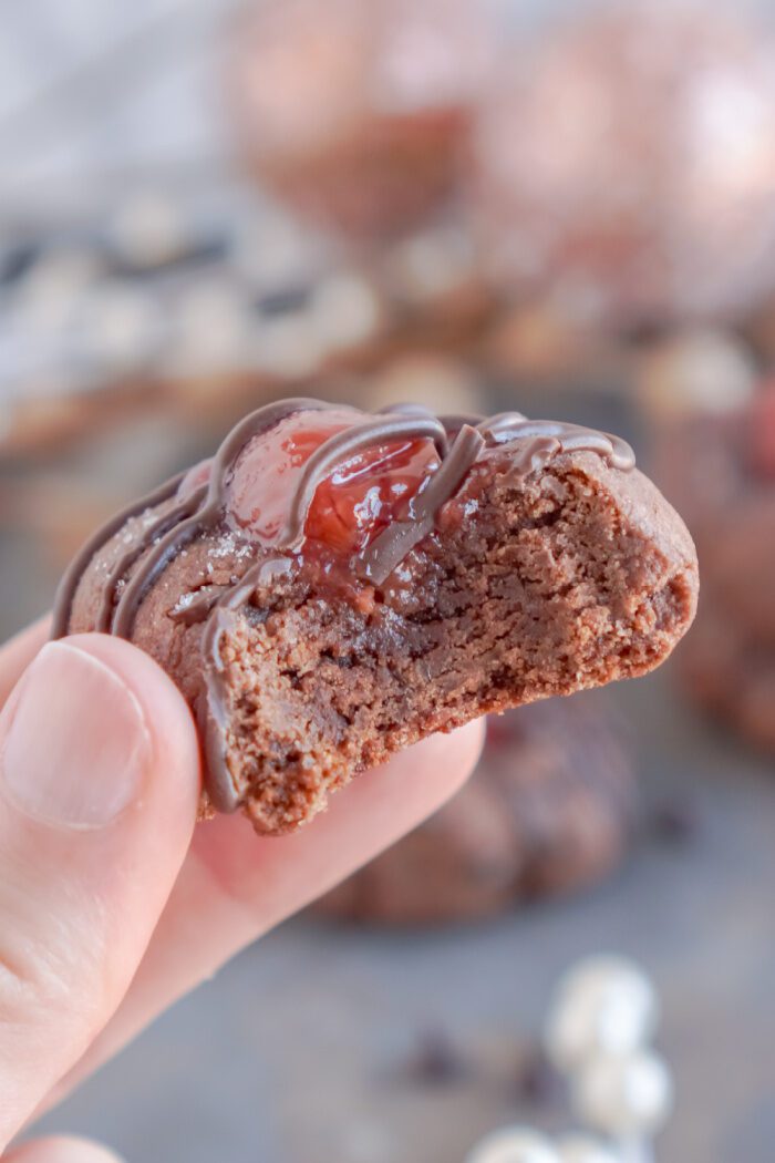 Someone holding a Chocolate Cherry Thumbprint Cookie with a bite taken out of it