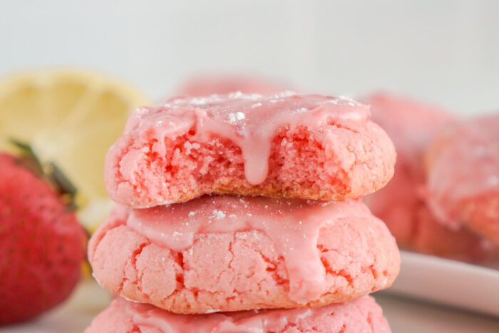 A stack of three strawberry sugar cookies with pink icing.