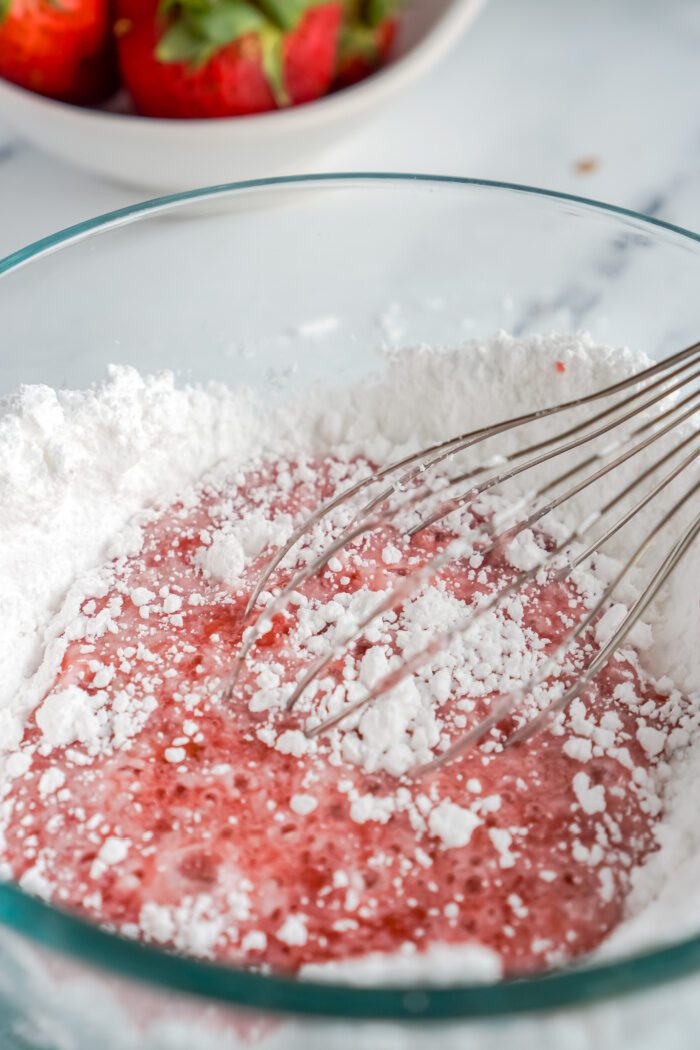 Mixing strawberry gelatin and powdered sugar in a bowl.