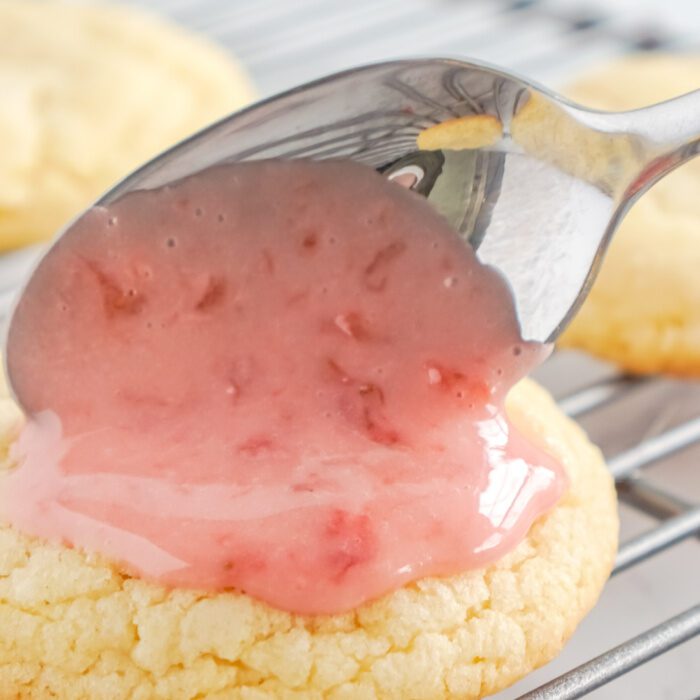 Spooning pink icing onto a sugar cookie.