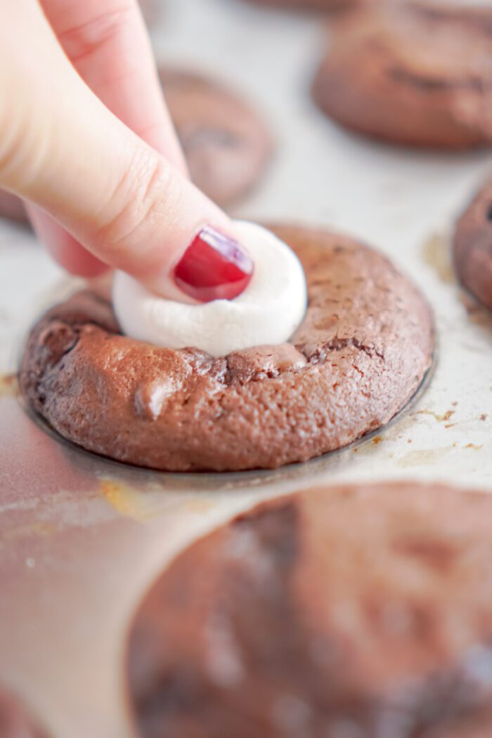 Someone pressing a marshmallow into a Hot Chocolate Cupcake