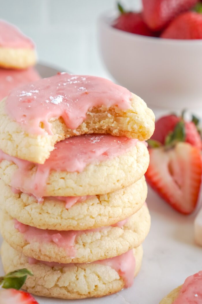 A stack of four strawberry sugar cookies with pink icing.