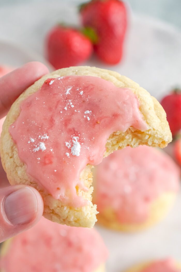 A hand holding a bitten strawberry sugar cookie.