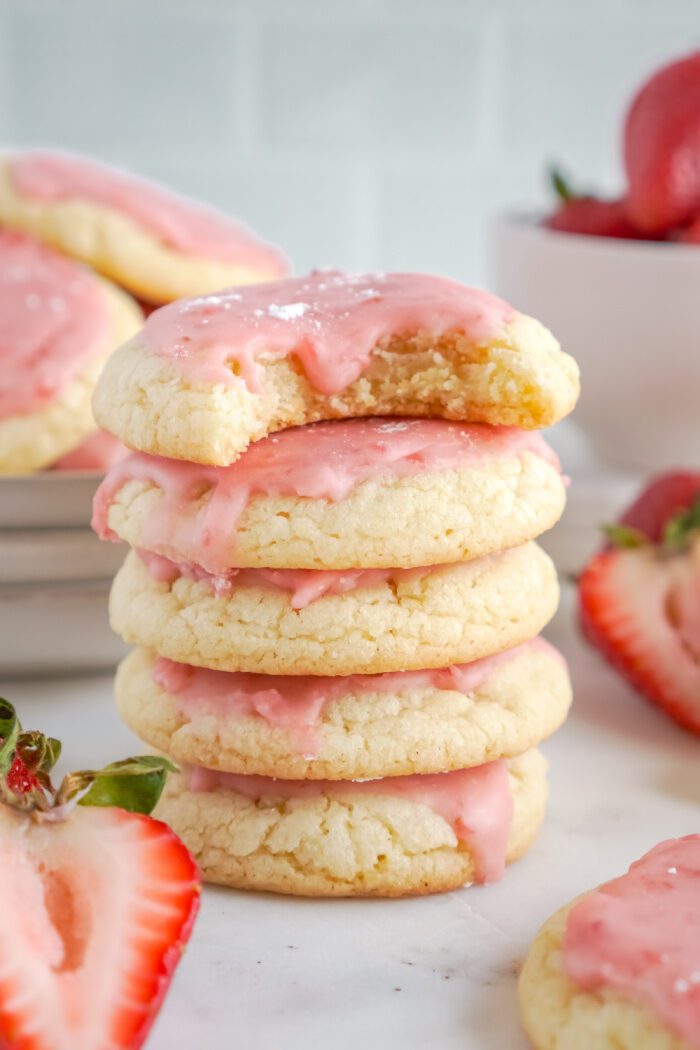 A stack of four strawberry sugar cookies with pink icing.