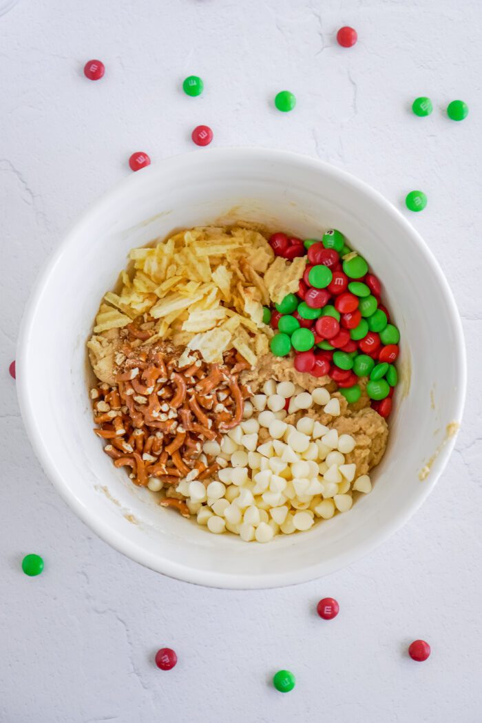 White chocolate chips, crushed potato chips, M&Ms, and pretzels added to bowl