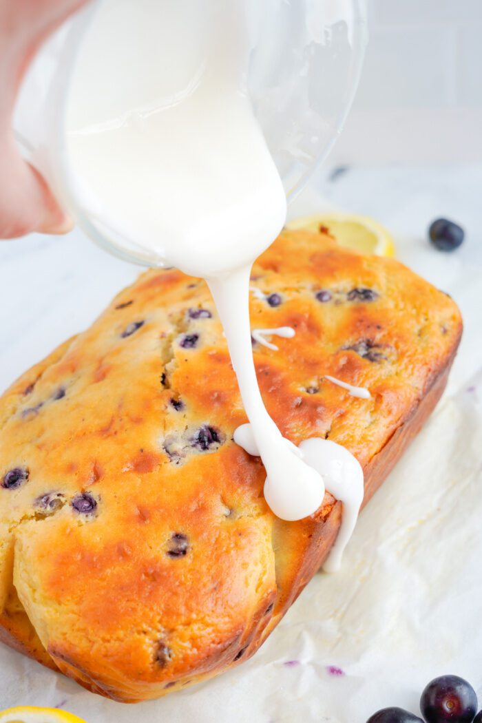 Pouring glaze over lemon blueberry loaf